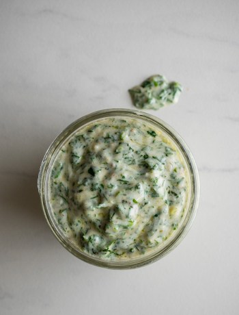 Overhead view of green goddess dressing in a jar with a small spill.