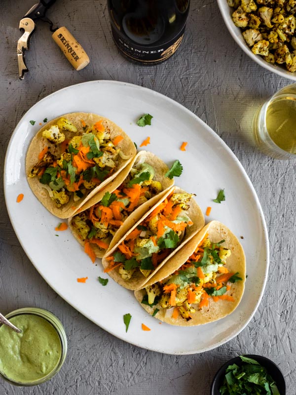 A plate of four curry roasted cauliflower tacos garnished with cilantro and grated carrots.